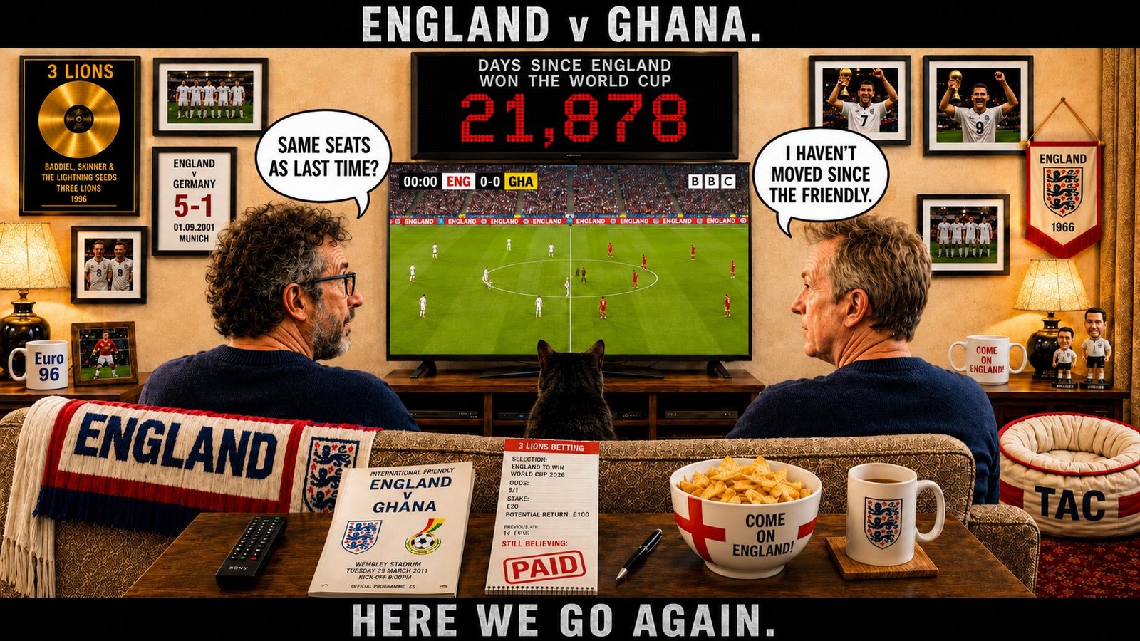 Top bar text: "ENGLAND v GHANA." In the England sofa room before kick-off, David Baddiel sits on the left and Frank Skinner on the right, with Tac between them facing the television. Baddiel asks, "SAME SEATS AS LAST TIME?" Skinner replies, "I HAVEN'T MOVED SINCE THE FRIENDLY." The television shows the teams at 0-0 before the match. Above it, the counter reads DAYS SINCE ENGLAND WON THE WORLD CUP: 21,878. The room includes the Three Lions gold disc, England memorabilia, the 2011 England v Ghana programme, a STILL BELIEVING betting slip and the COME ON ENGLAND bowl. Bottom bar text: "HERE WE GO AGAIN."